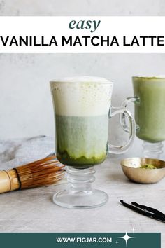 two mugs filled with green liquid next to a brush and spoon on a table