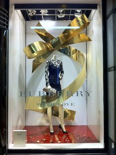 a mannequin in a display case with gold ribbon