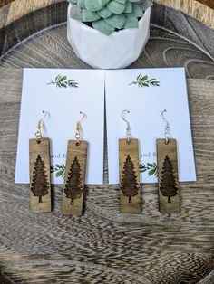 three wooden earrings with trees on them are sitting next to a card and potted plant