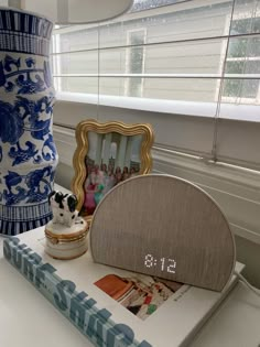 there is a blue and white vase sitting on the table next to a small clock