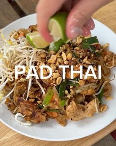 a person is picking up some food from a white plate with the words pad thai on it