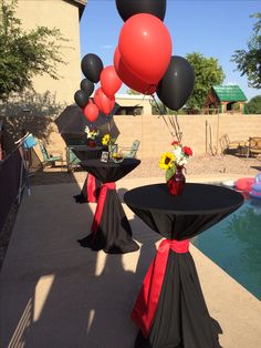 some black and red tables with balloons in the air near a swimming pool at a party