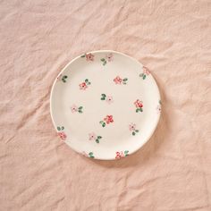 a white plate with pink and green flowers on it sitting on top of a bed