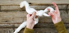 two hands holding white yarn in front of wooden planks