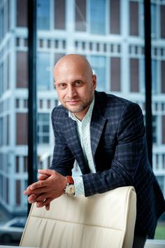 a bald man in a suit leaning on a chair