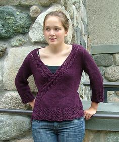 a woman standing next to a stone wall with her hands on her hips and looking at the camera