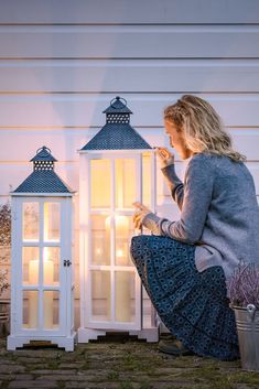 a woman sitting on the ground next to two white lanterns with lit candles in them