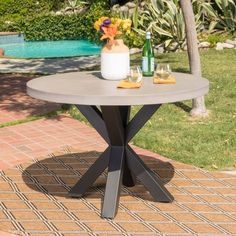 an outdoor table with flowers and bottles on it next to a swimming pool in the background