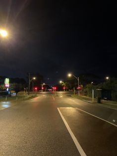 an empty street at night with lights on and no cars driving down the road in front of it