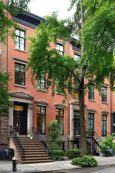 two people are sitting on the steps in front of some brownstone townhouses with trees and bushes