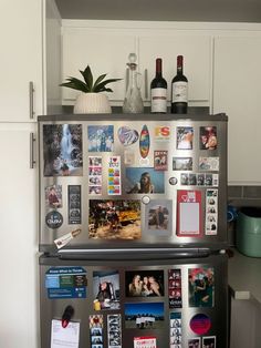 a refrigerator covered in magnets and pictures with wine bottles on the top, next to a potted plant