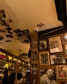 a room with many framed pictures on the wall and lights hanging from the rafters