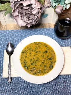 a white bowl filled with soup on top of a blue place mat next to a silver spoon