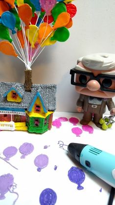 a small toy house next to a balloon tree and a marker pen on a table