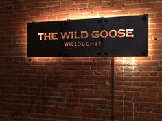 a sign that reads the wild goose in front of a brick wall with a light on it