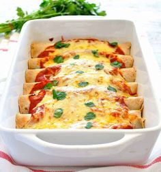 a white casserole dish filled with cheese and tomato sauce, garnished with fresh basil