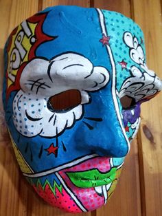 a blue mask with cartoon characters painted on it sitting on a wooden floor next to a pair of scissors