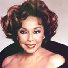 an old photo of a woman smiling at the camera with her hair pulled back and wearing earrings