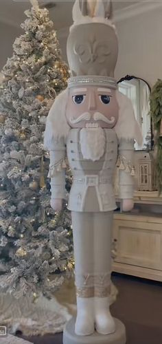 a statue of a nutcracker stands in front of a christmas tree