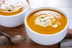 two white bowls filled with soup on top of a cutting board next to spoons