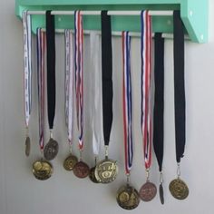 five medals are hanging on a green shelf with hooks and clips to hang them from the wall