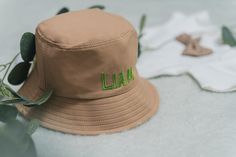 a tan hat with the word lain embroidered on it sitting next to some leaves