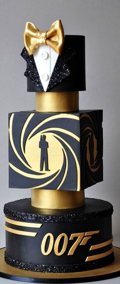 a black and gold cake with a golden bow tie on it's top tier