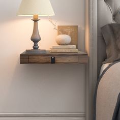 a nightstand with a lamp and some books on it next to a bed in a bedroom