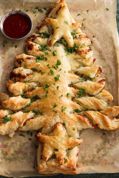 a christmas tree made out of pastry on a piece of parchment paper next to a bowl of ketchup