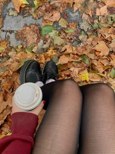 a woman is sitting on the ground with her legs crossed and holding a coffee cup