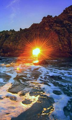 the sun is setting over an ocean with rocks in the background and foamy water