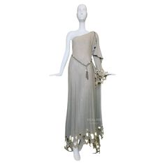 Stunning extremely rare Thierry Mugler Goddess Gown from one of his earliest Collections ca.1979. A masterful embodiment of ethereal elegance and avant-garde artistry. The dress cascades gracefully, draping effortlessly over the body. It can be worn either symmetrical or asymmetrical over one shoulder, the silhouette is both a nod to classical Grecian styles and a bold statement of modern femininity, capturing the duality of strength and delicacy that defines Mugler's aesthetic. Very soft, muted grey/champagne jersey cotton blend fabric. Highlight is the exquisite cutwork that adorns the hem and sleeves. These intricate patterns, meticulously edged in metallic gold thread, create a delicate interplay of light and shadow, transforming the fabric into a shimmering tapestry of opulence. Each Thierry Mugler Couture, Goddess Gown, Silk Evening Gown, Gucci Dress, Thierry Mugler, Cut Work, Corset Top, Black Silk, Timeless Beauty