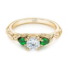 an antique style engagement ring with three green stones on the side and a round diamond center