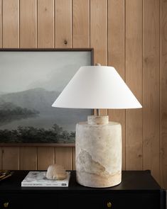 a white lamp sitting on top of a table next to a book and a painting