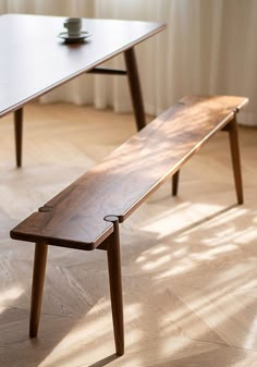 a wooden bench sitting on top of a hard wood floor next to a white curtain