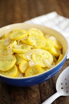 a blue bowl filled with sliced up bananas on top of a wooden table next to a spoon