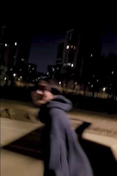 a blurry image of a man walking down the street at night with city lights in the background