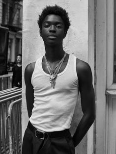 a young man standing in front of a building wearing a white tank top and black pants