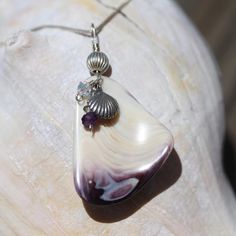 This is the first of many to come of our new line of beach jewelry. The designer collected various clam shells off the coast of New Jersey and hammered them apart into unique shapes. The shells have been through a variety of tumbling cycles and a final polish to bring this piece to a beautiful luster. Notice the purple throughout this piece which is also known as Wampum for the beautiful purple color. This piece was delicately wrapped in sterling silver wire to show off its beauty. The pendant m Ocean-inspired Abalone Shell Decor, Ocean-inspired Abalone Shell For Beach, Unique Silver Shell Necklace For Beach, Beach Shell-shaped Necklace With Natural Stones, Ocean-inspired Shell Necklace With Natural Stones, Clam Shells, Unique Shapes, Clam Shell, New Line