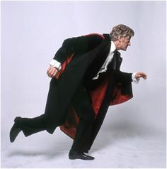 a man in a black suit and red cape is dancing with his hands on his hips