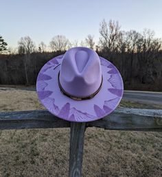 This hand burnt lavender wide brim fedora makes a perfect addition to any wardrobe. The lavender material burns a gorgeous shade of purple allowing the design to stand out. Each mountain is intricately burned by hand with a pyrography machine using various tips to achieve depth and a rock-like texture. Pine trees are burnt in front of the mountains creating a beautiful landscape. The design is original and completely freehanded. For a finishing touch the hat is adorned with a embroidered tie-back hat band with a gold feather embellishment. Hat Materials: polyester/cotton Hat circumference: 57-60 cm Hat Brim: Roughly 3.75 inches  Hat fits most with an adjustable tie hat band inside. Disclaimer: Colors may vary slightly from screen to screen. Hat fits most with an adjustable tie band inside Burned Hat Mountains, Feather Embellishment, Hat Burning, Mountain Hat, Cottagecore Gifts, Hat Western, Embroidered Tie, Lavender Sweater, Cowgirl Gifts