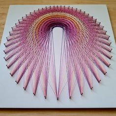 an art piece made out of pink and yellow yarn on top of a white board