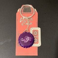 a bottle cap keychain with a purple flower on it and a coca - cola logo