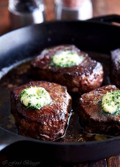 four steaks are cooking in a skillet with butter and broccoli on top