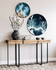 two vases sitting on top of a wooden table in front of a wall mounted painting