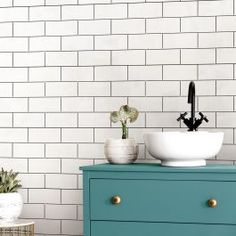 a white bowl sitting on top of a blue dresser next to a potted plant