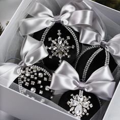 three black and white decorated cookies in a box with silver ribbon on the top, surrounded by pine branches