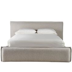 an upholstered bed with white linens and pillows on the headboard is shown