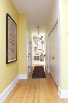 an empty hallway with yellow walls and pictures hanging on the wall, along with wooden flooring