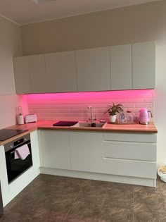 a kitchen with white cabinets and pink lighting